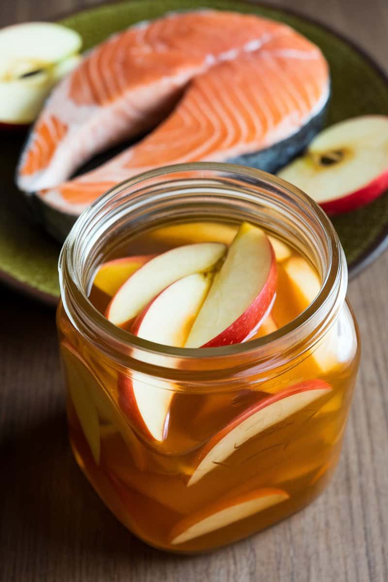 A jar of apple cider vinegar with apple slices, next to a fresh salmon fillet.