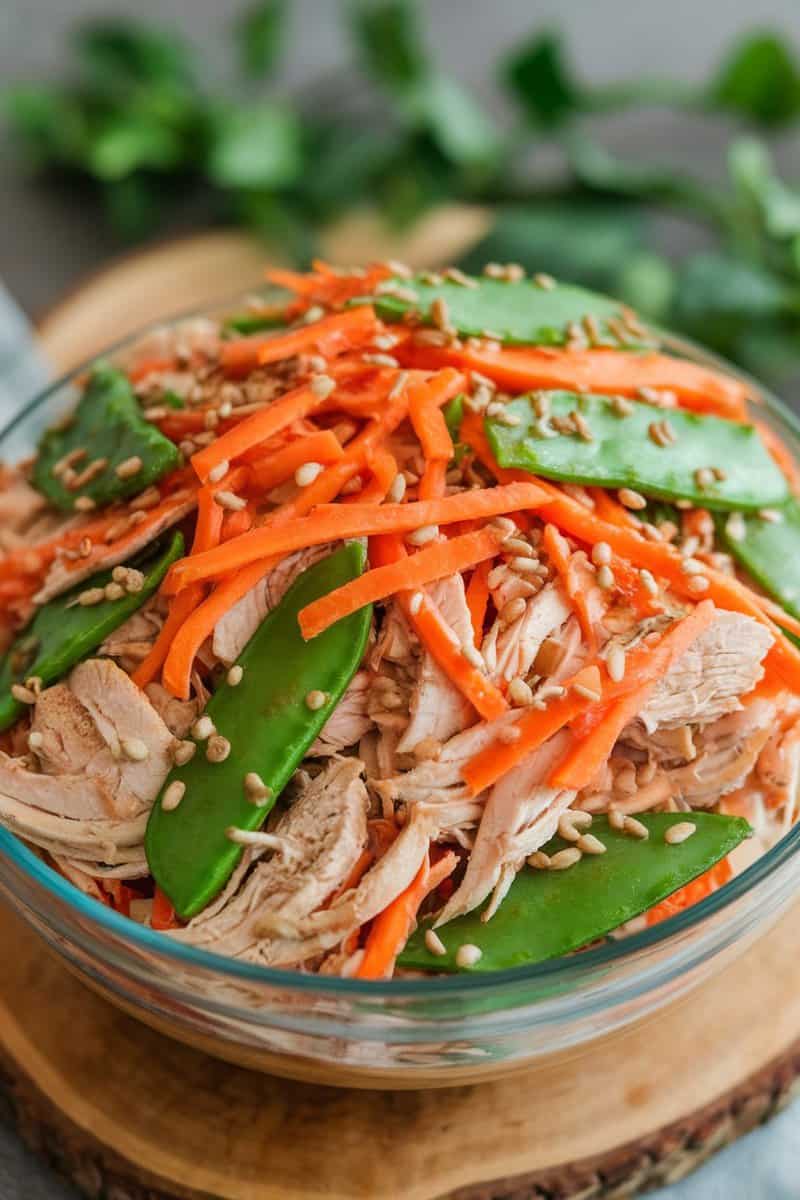 A vibrant bowl of Asian-inspired chicken salad featuring shredded chicken, carrots, and sugar snap peas.