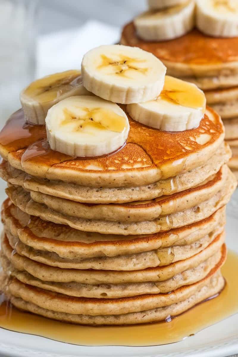 Stack of banana oatmeal pancakes topped with banana slices and syrup