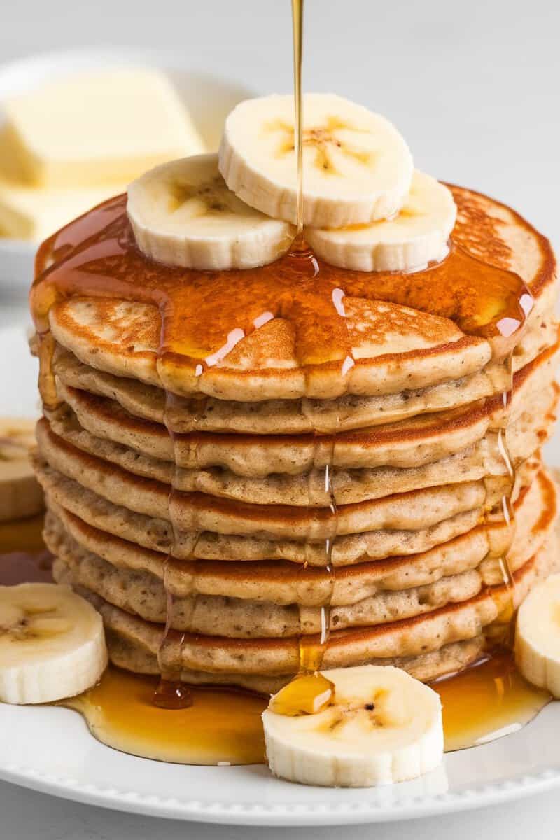 A stack of banana oatmeal pancakes topped with banana slices and maple syrup.