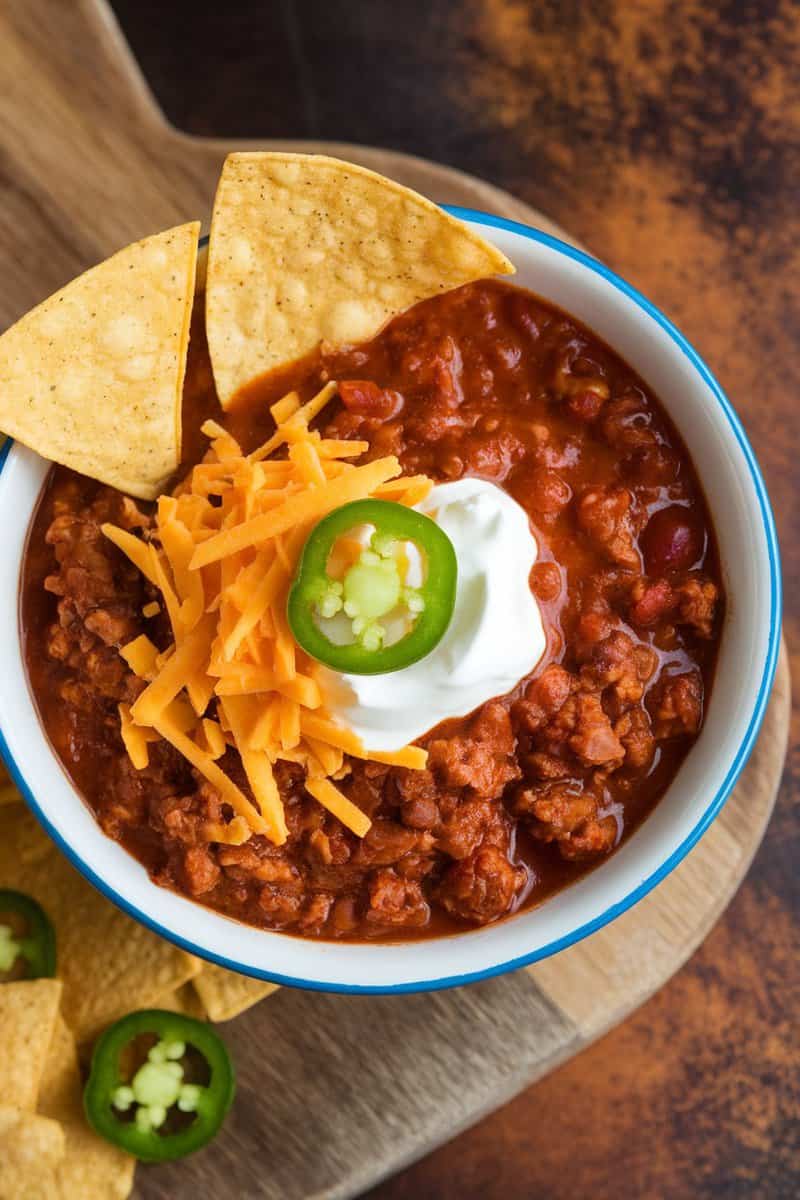 A bowl of classic beef chili topped with cheese, sour cream, and jalapeños, served with tortilla chips.