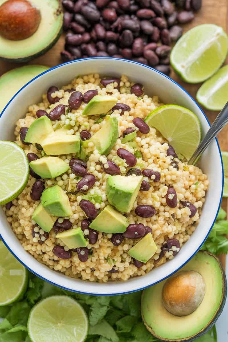 A bowl of couscous topped with black beans and avocado, garnished with lime.