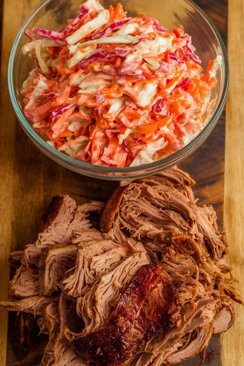 A bowl of creamy sriracha coleslaw, made with shredded cabbage and carrots, in front of a serving of pulled pork.