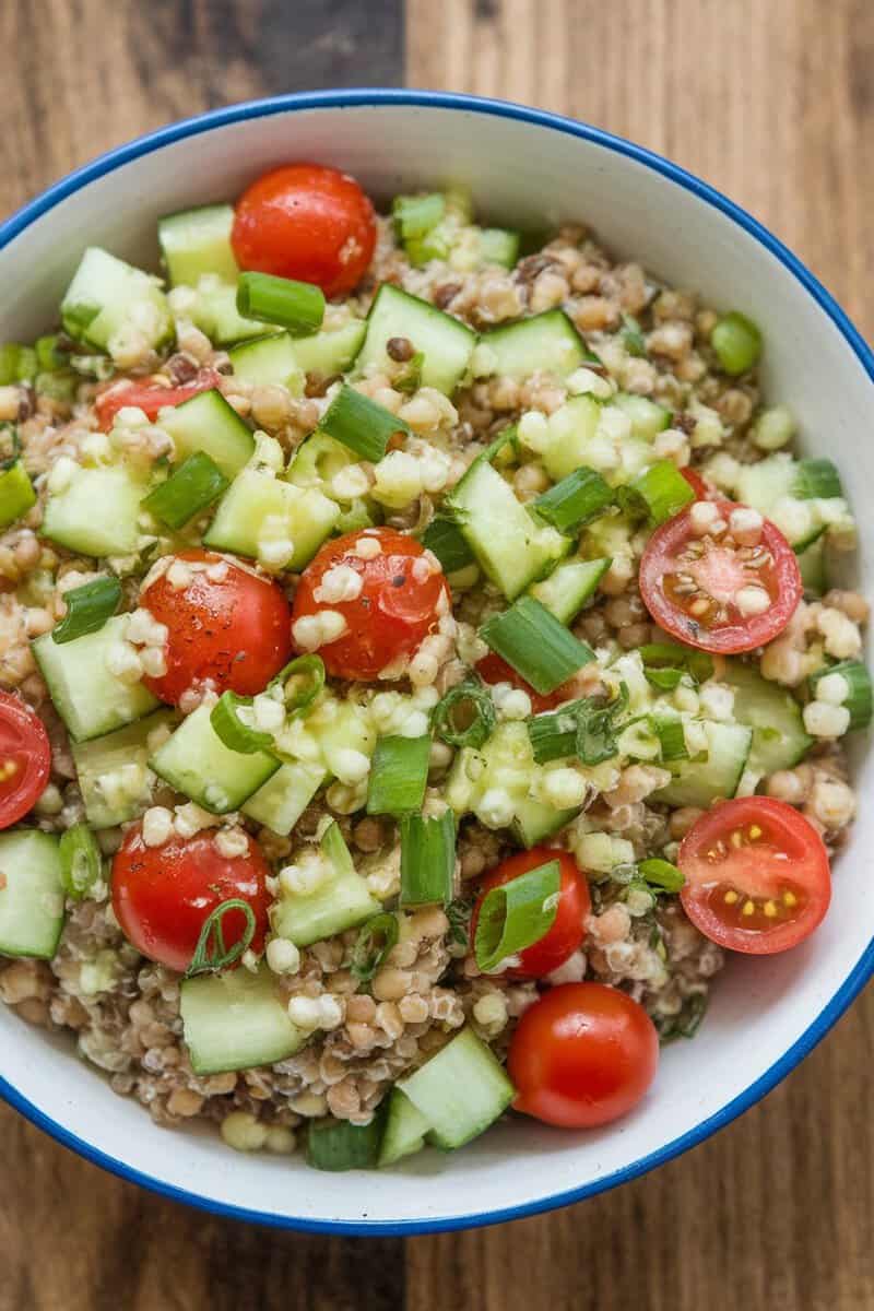 A bowl of Herbed Lentil Quinoa Salad with cherry tomatoes, cucumbers, and green onions