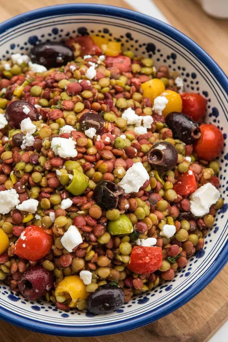 A colorful Mediterranean lentil salad with feta cheese, olives, and cherry tomatoes in a bowl.