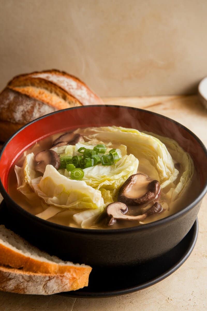 A bowl of napa cabbage and mushroom soup with green onions and slices of bread