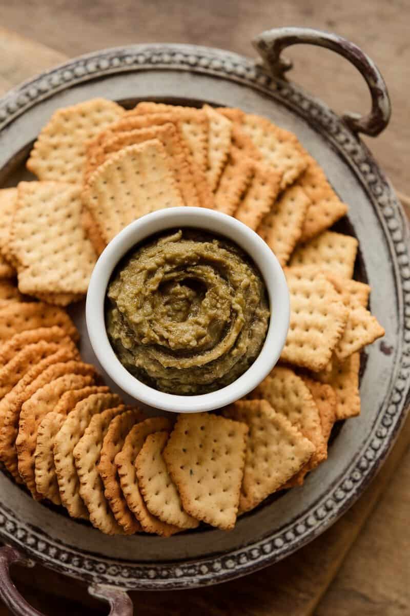 A bowl of olive tapenade surrounded by keto crackers on a decorative plate.