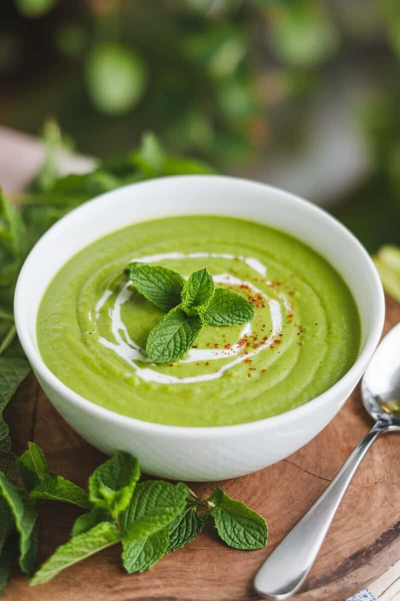 Bowl of vibrant green pea and mint soup garnished with mint leaves.