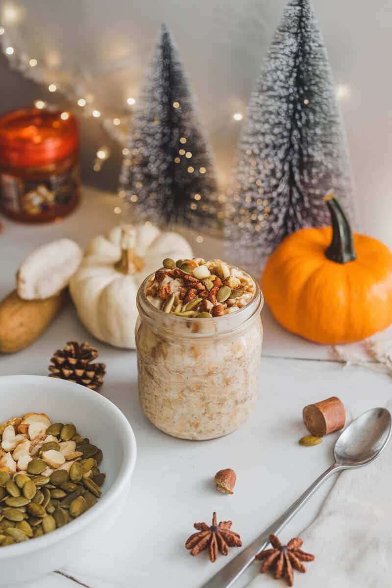 A jar of pumpkin spice overnight oats with nuts on top and pumpkin decorations around it.