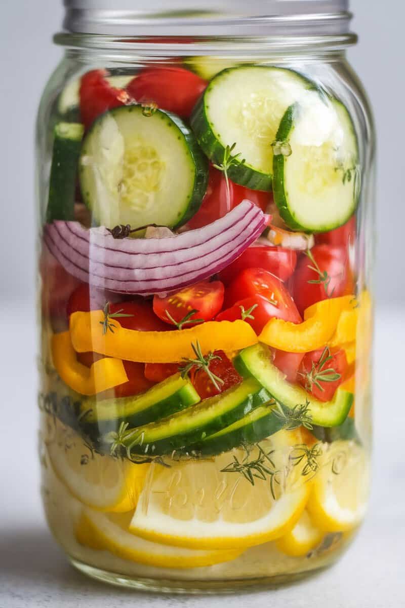 A layered jar of lemon cucumber salad with colorful vegetables and lemon slices.