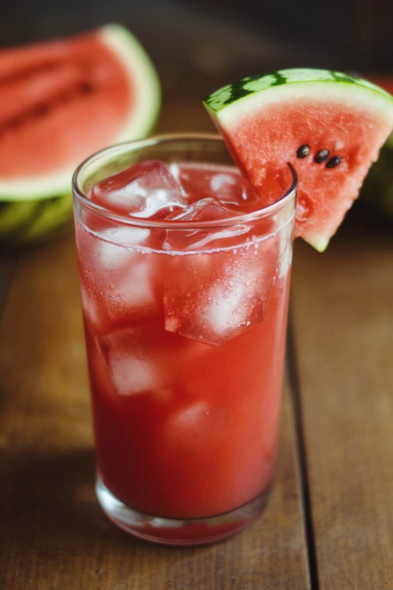 A refreshing watermelon cooler in a glass with ice and a slice of watermelon on the rim.