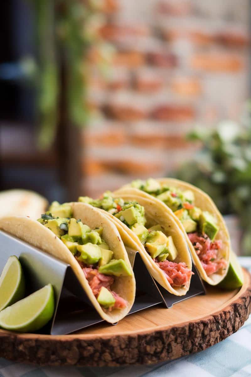 Three sesame tuna tacos topped with avocado salsa, served with lime wedges.