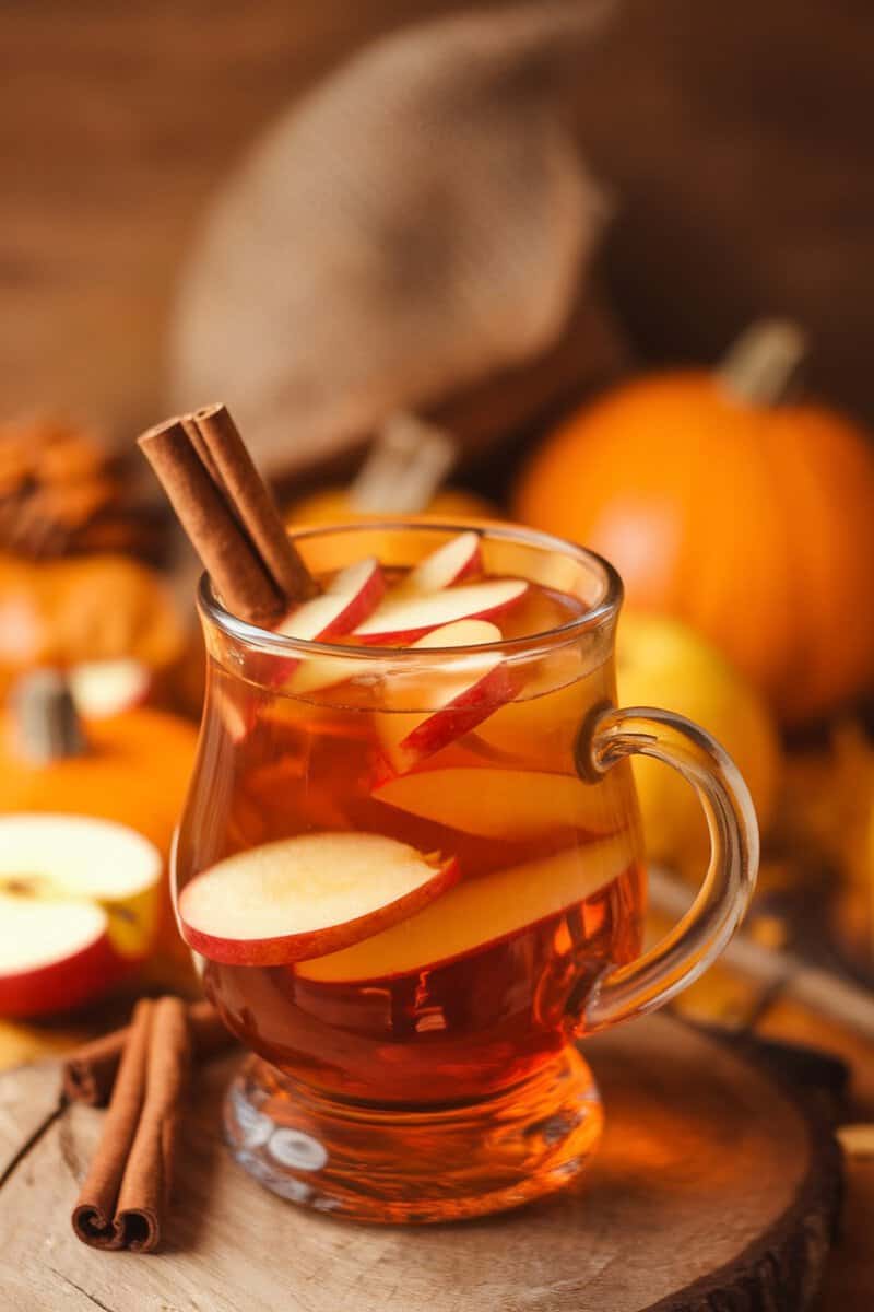 A glass of spiced apple cider with apple slices and cinnamon sticks