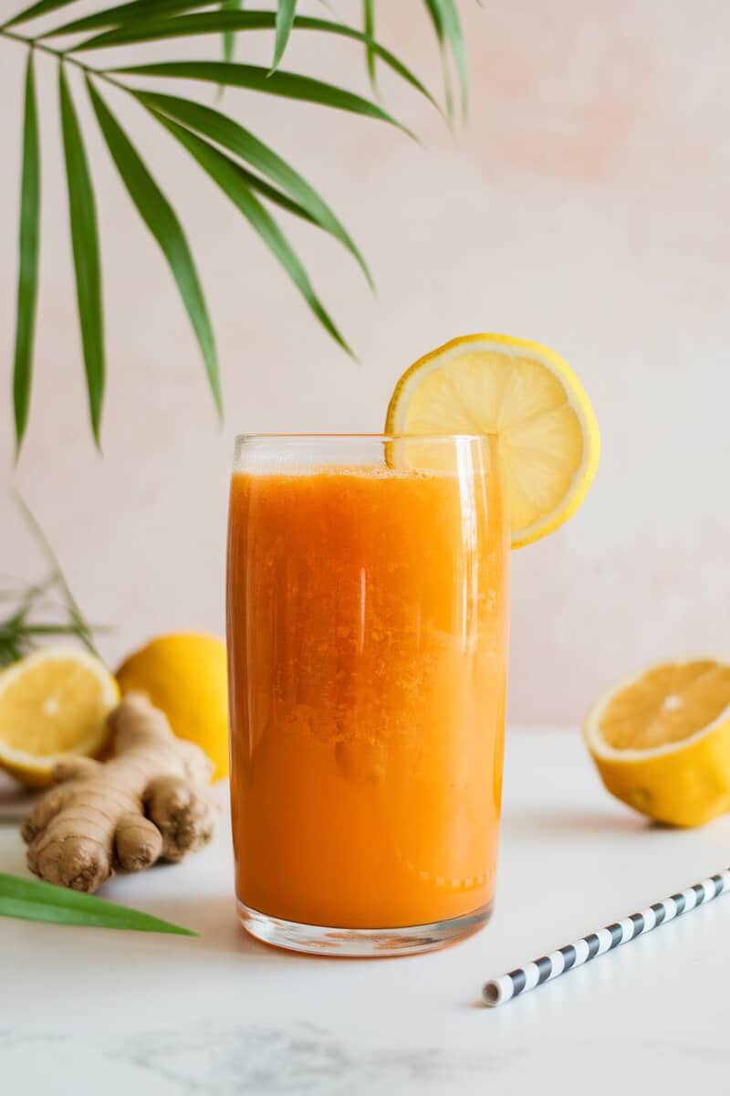 A glass of spicy ginger citrus juice with lemon slices and ginger root in the background.