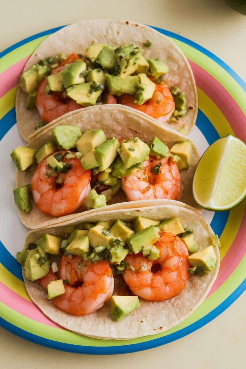 Three spicy shrimp tacos topped with avocado salsa on a colorful plate.