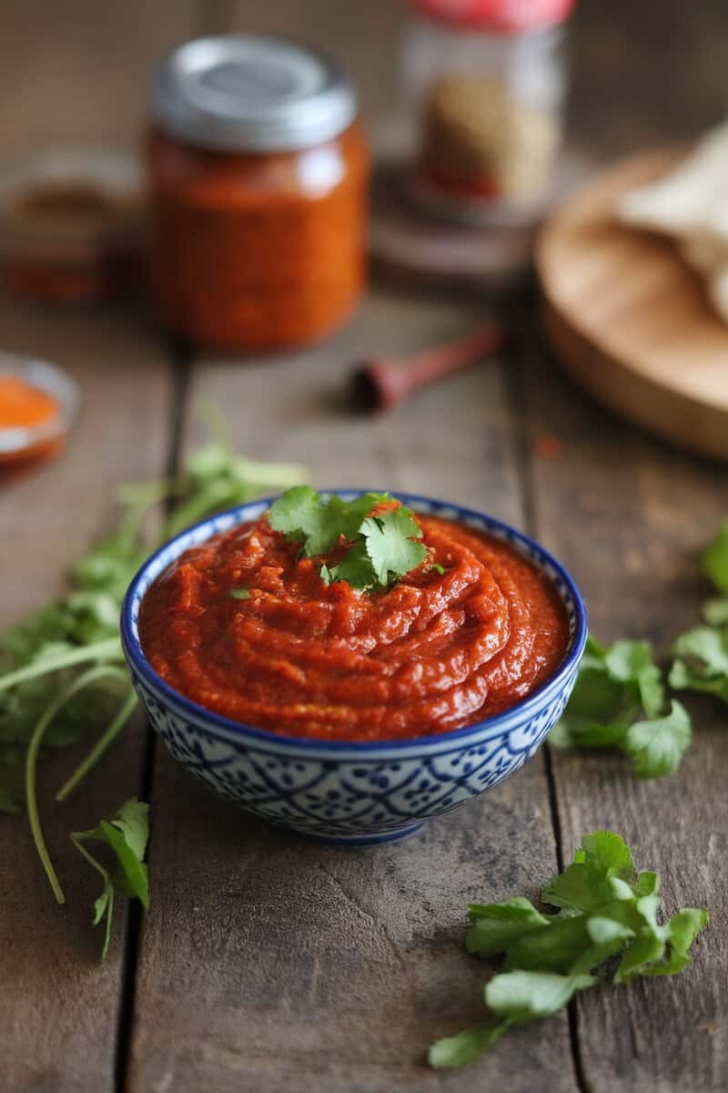 A vibrant bowl of spicy tomato and tamarind chutney garnished with coriander leaves, surrounded by fresh ingredients.