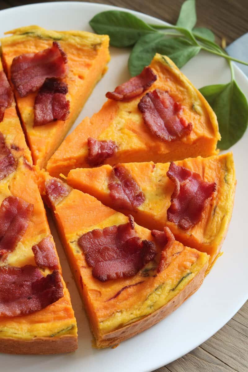 A sliced sweet potato and bacon frittata on a white plate, garnished with spinach.