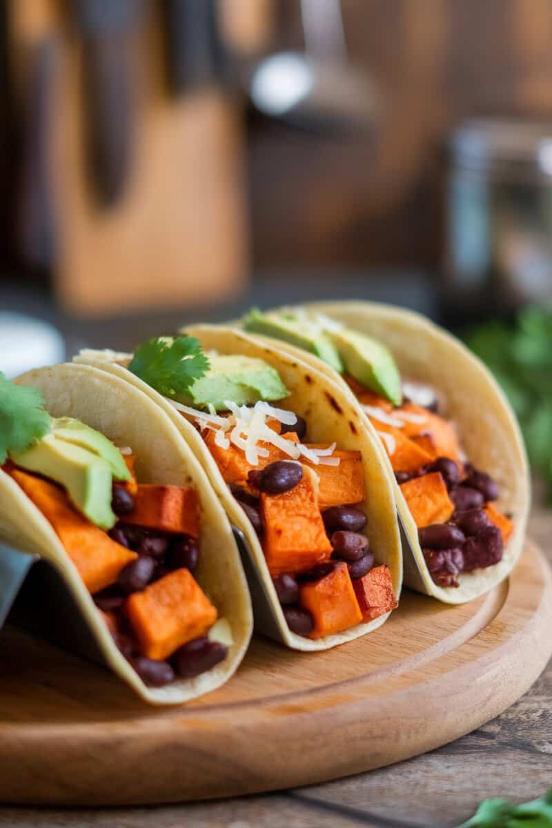 Sweet potato and black bean tacos on a wooden platter with avocado and cilantro