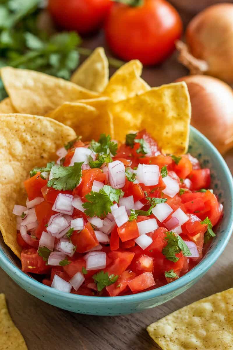 A bowl of fresh tomato salsa topped with diced onions and cilantro, served with tortilla chips