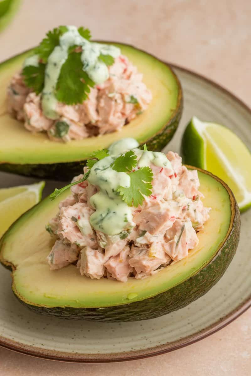 A fresh tuna-stuffed avocado topped with cilantro lime dressing and garnished with lime wedges.