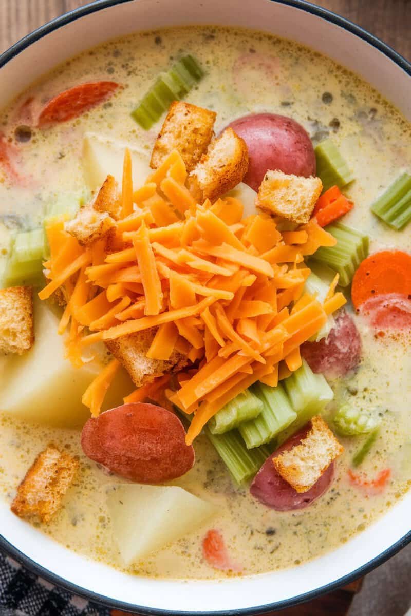 A bowl of vegetable chowder with cheddar, featuring carrots, celery, potatoes, and croutons.