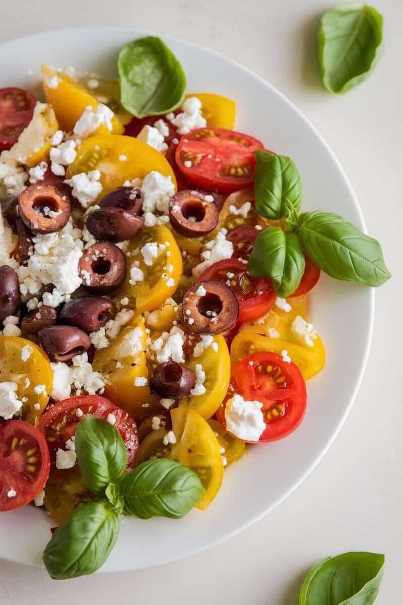 A colorful salad featuring yellow tomatoes, feta cheese, olives, and fresh basil.