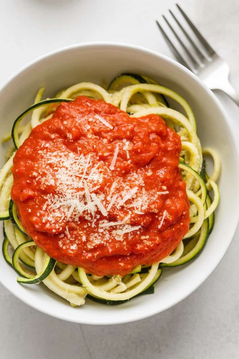 A bowl of zucchini noodles topped with marinara sauce and sprinkled with cheese.