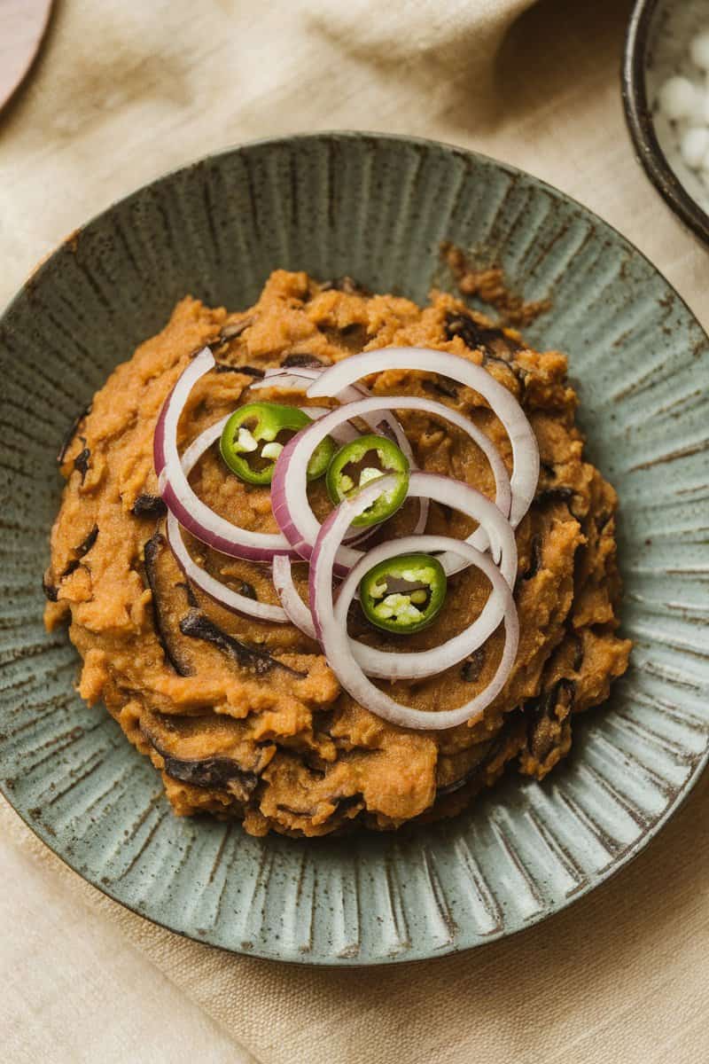 A bowl of Baingan Bharta, a smoky mashed eggplant dish, garnished with onions and green chilies.