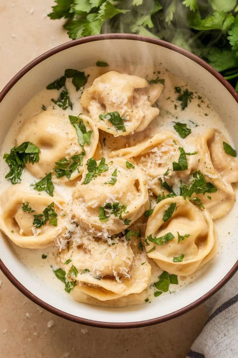 A bowl of creamy garlic chicken tortellini garnished with parsley.