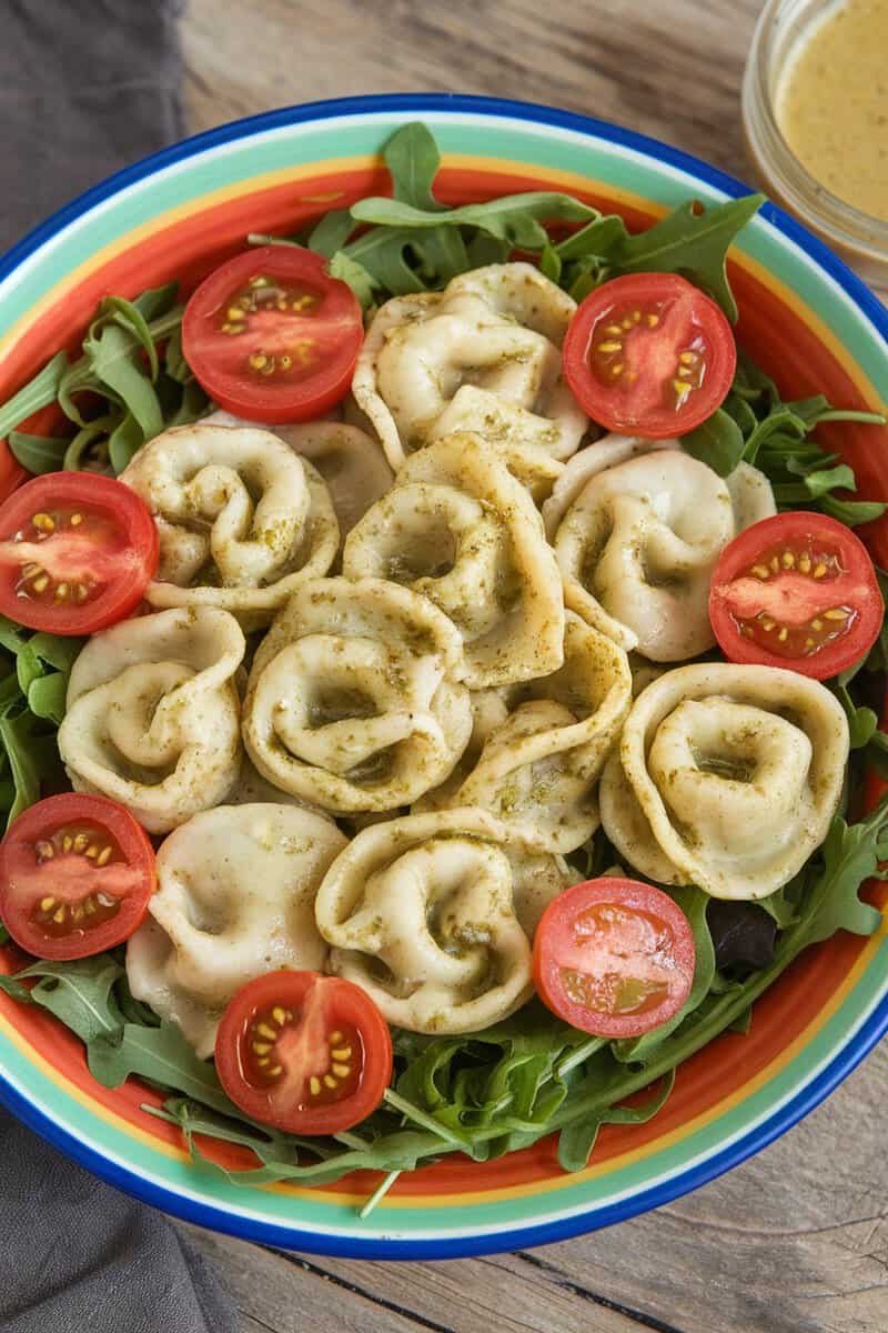 A colorful bowl of Pesto Chicken Tortellini Salad with mixed greens and cherry tomatoes.